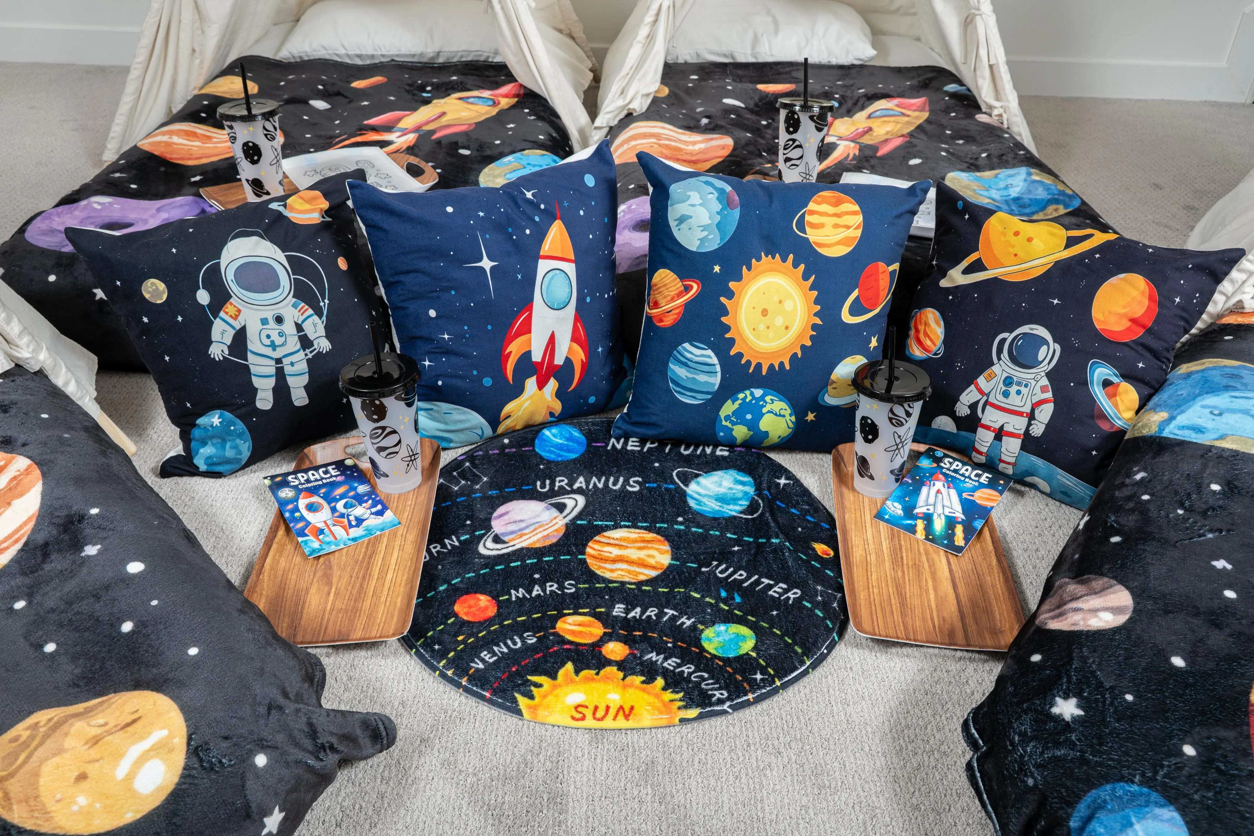 Space-themed teepees arranged around a planet-print rug, with astronaut cushions and trays.